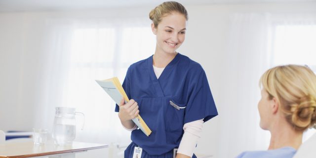 Nurse with medical records talking to patient in hospital room